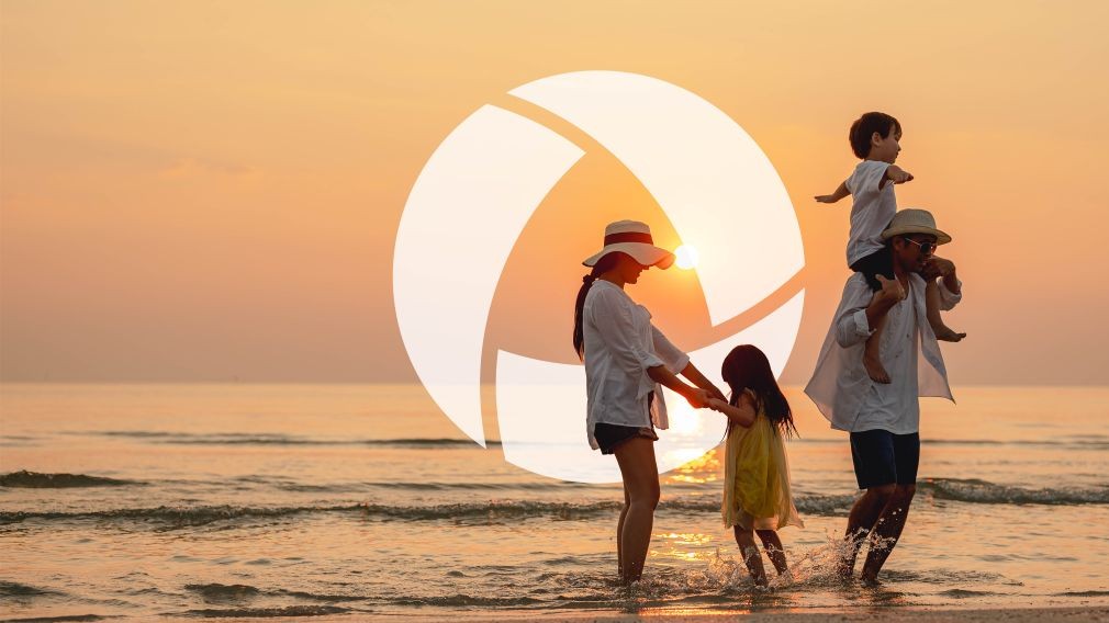 Family of four standing on a beach surrounded by water in front of sunset with Absolute Total Care logo in background